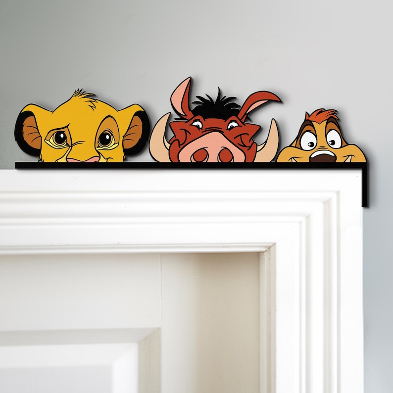 May include: A decorative door topper featuring Simba, Pumbaa, and Timon from The Lion King. The characters are in vibrant colors, with Simba in yellow, Pumbaa in reddish-brown, and Timon in tan. The topper is mounted on a black bar.