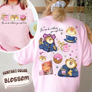 May include: Pink Comfort Color t-shirt with a cartoon leopard design. The front features a coffee cup, leopard face, and donut. The back has a leopard in a police uniform, a donut, and the text "You can be whatever you wish to be."