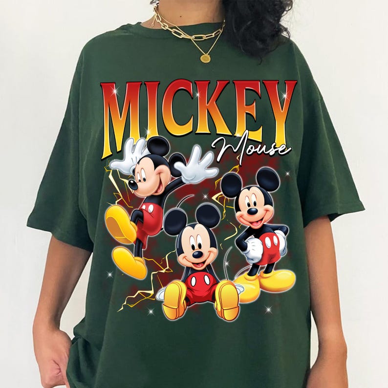 May include: Dark green t-shirt with a Mickey Mouse graphic. The design includes the word "MICKEY" in red and yellow, above "Mouse" in script. Mickey is depicted in several poses, wearing red shorts and yellow shoes.