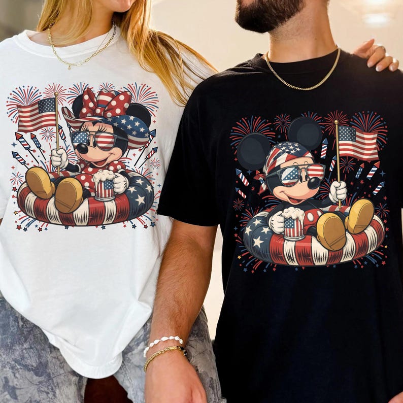 May include: White and black t-shirts featuring a cartoon mouse character in patriotic attire. The mouse is wearing sunglasses and holding an American flag and a mug. The design includes fireworks and a red, white, and blue inner tube.