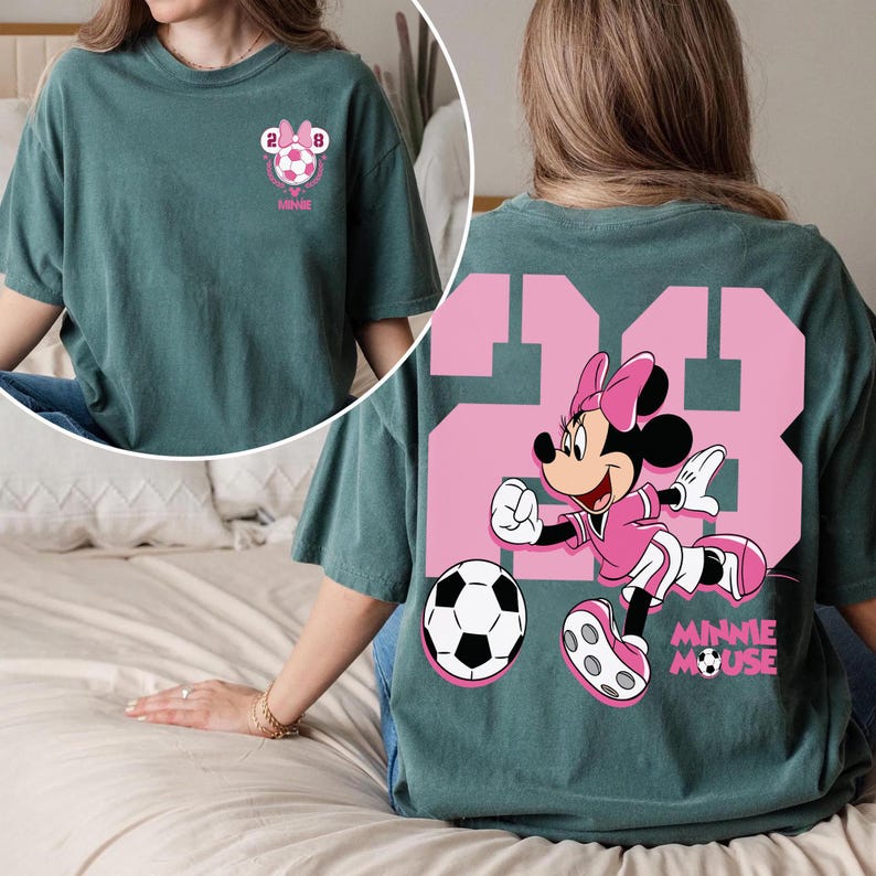 May include: Teal green t-shirt with a pink Minnie Mouse soccer design. The front has a small graphic with a soccer ball and the text "MINNIE". The back displays a large "23" with Minnie Mouse and a soccer ball, and the text "MINNIE MOUSE".