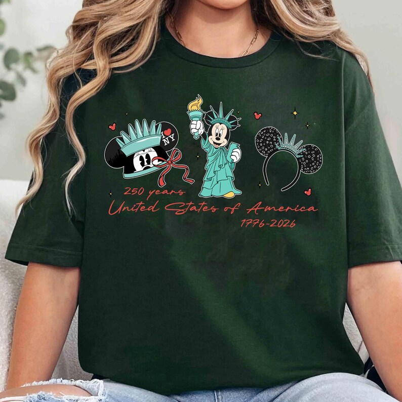 May include: Dark green t-shirt featuring Mickey Mouse as the Statue of Liberty, a Mickey Mouse ear headband, and a Mickey Mouse head with a crown. Text reads "250 years United States of America 1776-2026".