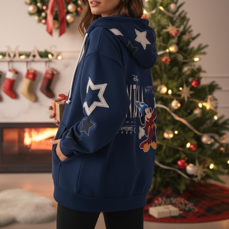 May include: Navy blue hooded sweatshirt with white star accents and a Mickey Mouse graphic on the back. The sweatshirt has a white drawstring and a kangaroo pocket. The design includes the text "Minnie's Appetite Key".