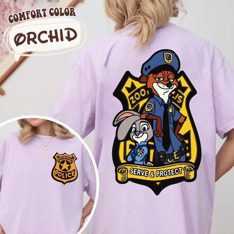 May include: Lilac t-shirt with a cartoon illustration of a fox and a rabbit in police uniforms, with the text "Zootopia Police" and "Serve & Protect". A smaller police badge is also visible on the front of the shirt.
