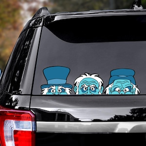 May include: A car window decal featuring three cartoon ghosts with blue skin and white hair. The ghosts are wearing hats and looking over the edge. The decal is applied to the rear window of a black SUV.