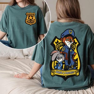 May include: Teal t-shirt with a Zootropolis Police badge on the front and a larger graphic on the back. The back graphic features Nick Wilde and Judy Hopps, with the text "Zootropolis Police" and "Serve & Protect".