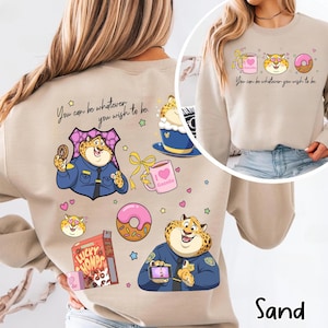 May include: Sand-colored sweatshirt featuring a cartoon cheetah character in a police uniform, holding a donut and a phone. The design includes a pink donut, a coffee cup, and the text "You can be whatever you wish to be."