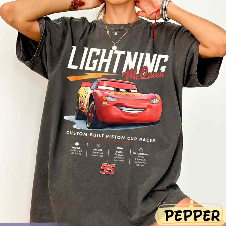 Puede incluir: Camiseta gris oscuro con un dise&ntilde;o de Rayo McQueen de la pel&iacute;cula Cars. El dise&ntilde;o incluye el texto "LIGHTNING McQueen" y "CUSTOM-BUILT PISTON CUP RACER". El n&uacute;mero "95" se muestra de forma destacada. La camiseta tiene un corte holgado.