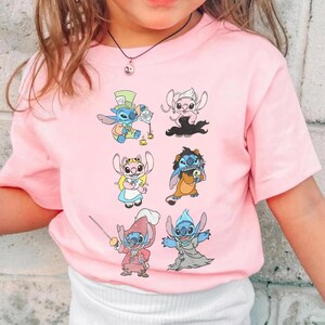 Puede incluir: Una camiseta de manga corta de color rosa claro con un estampado gr&aacute;fico de seis personajes de dibujos animados. Los personajes aparecen con diversos disfraces, como un anfitri&oacute;n de una fiesta de t&eacute;, un personaje rubio, un espadach&iacute;n y un fantasma.