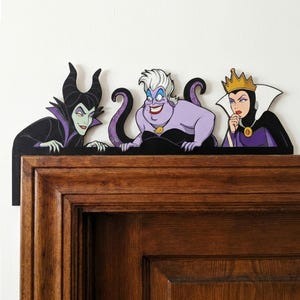 May include: Wooden decorative shelf featuring three cartoon villains: Maleficent, Ursula, and the Evil Queen. Maleficent is in black and purple, Ursula is purple, and the Evil Queen is in black and purple. The shelf is mounted on a wooden door frame.