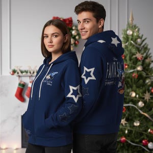 May include: Two people wearing navy blue zip-up hoodies. The hoodies feature white star designs on the sleeves and back, along with the text "Fantasia" and a Mickey Mouse graphic. A Christmas tree and decorations are in the background.