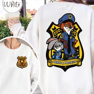 May include: White sweatshirt with a Zootropolis police badge on the front and a larger graphic on the back. The back graphic shows Nick Wilde and Judy Hopps in police uniforms, with the text "SERVE & PROTECT".