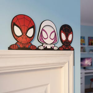 Puede incluir: Tres recortes de personajes de dibujos animados de Spider-Man, Spider-Gwen y Miles Morales. El recorte de Spider-Man es rojo y negro, Spider-Gwen es blanco y morado, y Miles Morales es negro y rojo. Están colocados encima de un marco de puerta blanco.