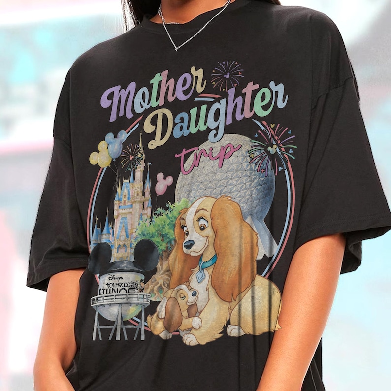 May include: Black t-shirt with a colourful graphic featuring the text "Mother Daughter Trip" and Disney characters. The design includes a castle, a globe, and the Lady and the Tramp dogs. The shirt has a relaxed fit.