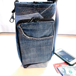 May include: A denim crossbody bag with a zippered pocket and a black strap. The bag is made from recycled denim and has a unique patchwork design.