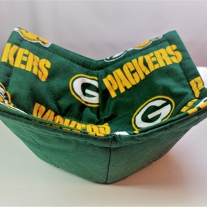 May include: Green and gold fabric bowl with the words "Packers" and "G" repeated on the fabric. The bowl is folded and ready to be used.