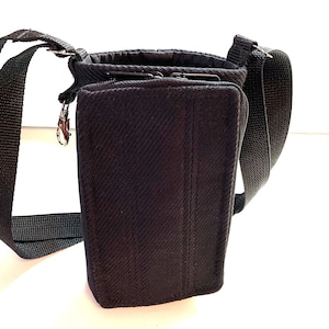 May include: A black canvas crossbody bag with a zippered closure and a small metal hook. The bag has a long adjustable strap.