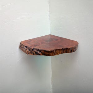 May include: A corner shelf made from a natural wood slice with a live edge. The shelf is mounted on a white wall and has a rustic, organic look.