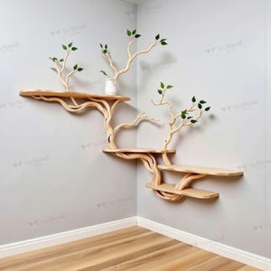 May include: A unique wooden wall shelf unit with a tree branch design. The shelves are light brown and have a natural wood grain. The branches support the shelves and have small green leaves attached. The unit is mounted on a gray wall.