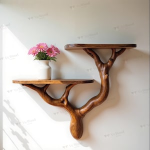 May include: A unique, handcrafted wooden wall shelf with two tiers, designed to resemble a tree. The natural wood grain is visible, and the shelf is holding a white vase with pink flowers. The shelf is mounted on a white wall.