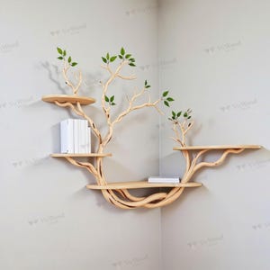 May include: A unique, light-colored wooden corner shelf designed to resemble a tree. The shelf has multiple circular platforms and branches, with green leaf accents. Books and a small stack of books are placed on the shelves.
