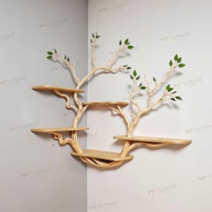 May include: A wooden tree-shaped wall shelf with multiple circular shelves. The light-colored wood has a natural grain, and the branches extend with green leaves. The shelf is mounted on a gray and white wall.