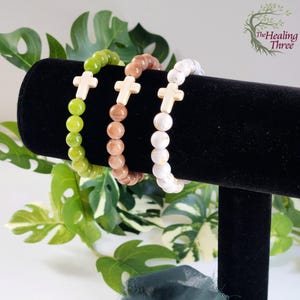 May include: Three beaded bracelets with gold cross charms. The bracelets are green, brown, and white.