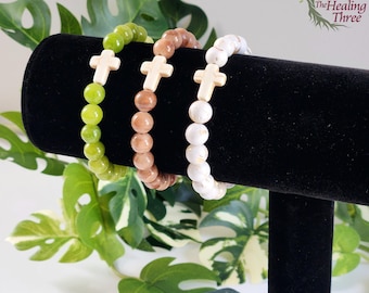 Op de afbeelding: Drie kralenarmbanden met gouden kruisbedels. De armbanden zijn groen, bruin en wit.