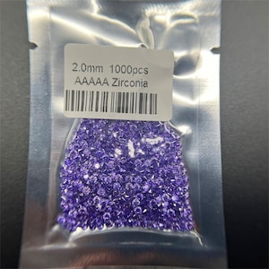 Könnte beinhalten: Nahaufnahme einer Tüte mit 1000 lilafarbenen 2,0 mm AAA Zirkonia-Steinen. Die Tüte trägt ein Etikett mit der Aufschrift "2,0 mm 1000pcs AAAAA Zirconia".