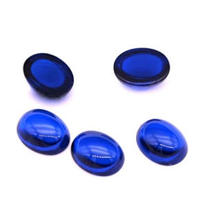 Puede incluir: Cinco piedras de vidrio ovaladas de color azul cobalto. Las piedras tienen una superficie lisa y brillante y una forma redondeada. Las piedras están dispuestas sobre un fondo blanco, con diferentes orientaciones. Las piedras son probablemente elementos decorativos o suministros para manualidades.