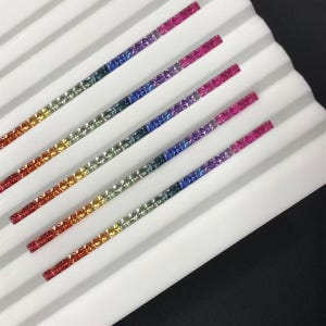 May include: A close-up shot of several thin, rectangular strips with a rainbow gradient. Each strip displays a spectrum of colours, from red to purple, set against a white, ridged background. The strips appear to be made of small, square-cut stones.