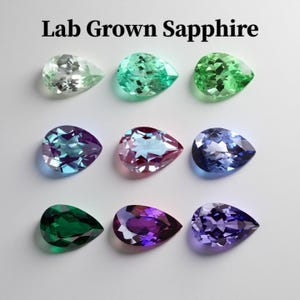 May include: Nine pear-shaped lab-grown sapphires in various colours are shown. The gemstones are arranged in three rows of three, with colours including green, blue, and purple. The text "Lab Grown Sapphire" is at the top.
