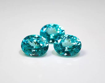 May include: Three oval-cut, teal-colored gemstones are displayed against a white background. The gems have a brilliant cut, reflecting light and showcasing their facets. The arrangement suggests a collection of precious stones, possibly for jewelry or crafting.