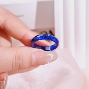 May include: A vibrant cobalt blue ring featuring a faceted, geometric surface texture. The band is constructed from a translucent material that catches the light, creating sharp angles and deep blue tones across its circular, multi-faceted exterior.