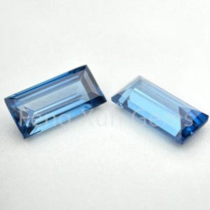 May include: Two rectangular blue gemstones with a faceted cut.