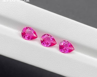 May include: Three vibrant, teardrop-shaped, pink gemstones are displayed on a white surface. The gems have a faceted cut, catching the light and showcasing their brilliant color. The arrangement highlights the gems' clarity and shape.