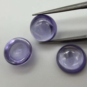 May include: Three round, cabochon-cut amethyst gemstones. The gemstones are a pale lavender colour and have a smooth, polished surface.