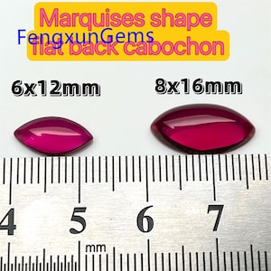 Puede incluir: Dos piedras preciosas en cabujón de forma marquesa, una que mide 6x12 mm y la otra 8x16 mm, se muestran en una regla. Ambas piedras son de un color rojo intenso y rico.