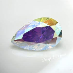 May include: A pear-shaped faceted gemstone featuring a deep purple center surrounded by iridescent, rainbow-like edges that reflect light. The surface of the stone displays the text "JengYunGems" in a white, cursive, semi-transparent font.