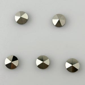 Könnte beinhalten: Fünf silberfarbene Metallnieten mit einem facettierten Design. Die Nieten sind symmetrisch auf einem weißen Hintergrund angeordnet.