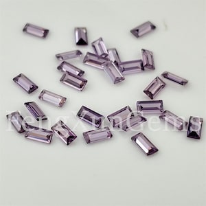 May include: A collection of small, rectangular, faceted purple gemstones scattered across a surface. Each stone features a clear, light violet hue with sharp, clean edges and a polished finish. The text FengXunGems is visible in white.