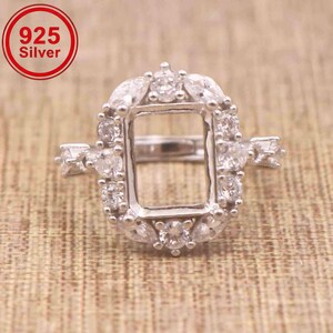 May include: A 925 silver ring setting featuring a rectangular centre opening surrounded by a halo of small, clear, round and marquise-cut stones. The metal band is polished silver, and the design includes additional small stones on the sides.