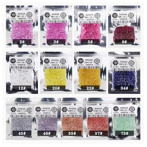 Może przedstawiać: Zestaw małych, kolorowych, okrągłych szklanych koralików w indywidualnych przezroczystych plastikowych torebkach. Każda torebka zawiera 1000 sztuk koralików i jest oznaczona numerem oraz tekstem "AAAA STAR 1000PCS STAR".