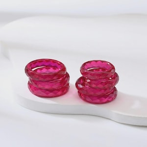 May include: Two stacks of vibrant fuchsia pink rings, each featuring a faceted, geometric surface texture. The rings are constructed from a translucent material, creating a bright, reflective appearance with sharp, angular edges throughout.