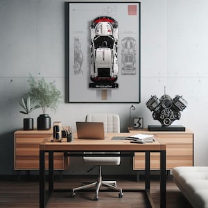 Könnte beinhalten: Ein weißes und rotes Lego Porsche 911 GT3 RS Modell-Auto, das an einer Wand mit einem Blaupausen-Design ausgestellt ist. Das Auto ist von einem schwarzen Rahmen und einem weißen Hintergrund umgeben. Ein schwarzes und silbernes Motormodell steht auf einem schwarzen Ständer auf einem Holztisch.