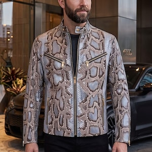 Peut inclure: Une veste à manches longues avec un motif peau de serpent dans des tons gris, bleu et marron. La veste présente un col montant avec un bouton-pression, une fermeture éclair intégrale et quatre poches zippées avec des détails dorés.