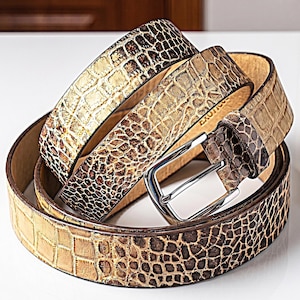 May include: A collection of coiled leather belts with a reptile skin pattern in shades of brown and tan. Each belt features a silver-colored buckle. The belts are arranged on a white surface.