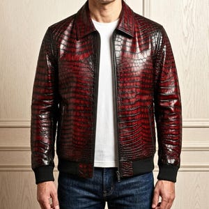 Puede incluir: Una chaqueta de manga larga con una textura de relieve de cocodrilo en rojo oscuro y negro, cuello en punta, cremallera frontal completa y puños y dobladillo acanalados en negro, usada sobre una camiseta blanca lisa.