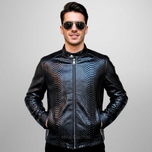 Könnte beinhalten: Schwarze Lederjacke mit Schlangenmuster. Die Jacke hat einen Reißverschluss, einen Stehkragen und zwei Vordertaschen. Die Jacke wird von einer Person mit Sonnenbrille getragen.