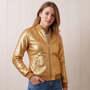 May include: A metallic gold bomber jacket featuring a textured snakeskin-like pattern, a front zipper closure, long sleeves with ribbed cuffs, a ribbed collar, and two side pockets. The jacket is worn over a plain white shirt and blue denim jeans.